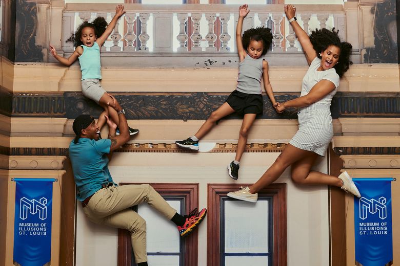 A family hands from the front of a building in an optical illusion at the Museum of Illusions St. Louis.