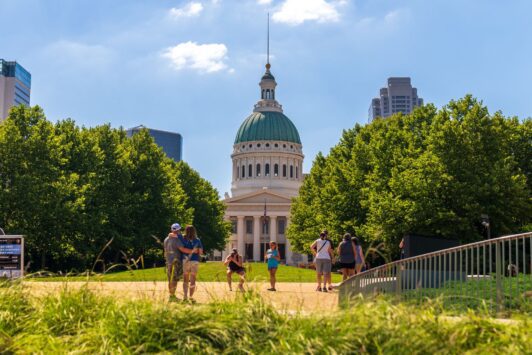 Visitors take photos in Gateway Arch National Park with the Old Courthouse in the background.